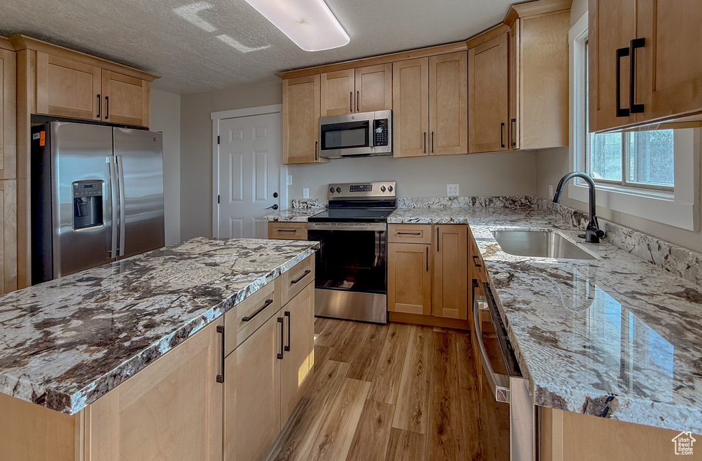 Kitchen with stainless steel appliances, light wood-type flooring, light stone counters, light brown cabinetry, and a kitchen island