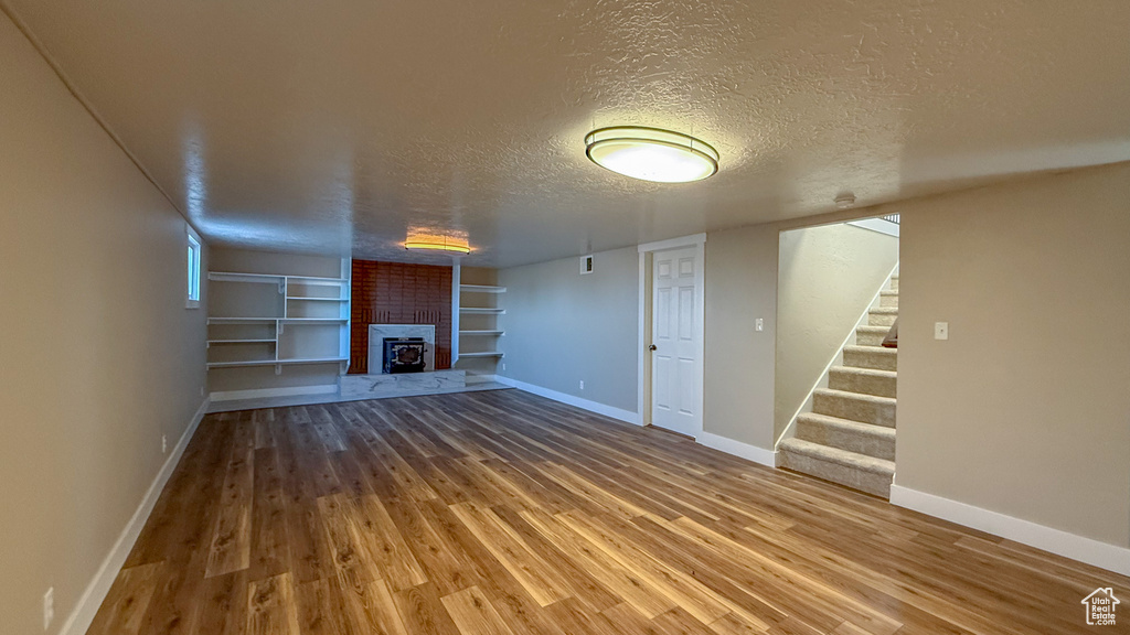 Unfurnished living room with a textured ceiling, a brick fireplace, built in shelves, wood finished floors, and stairway