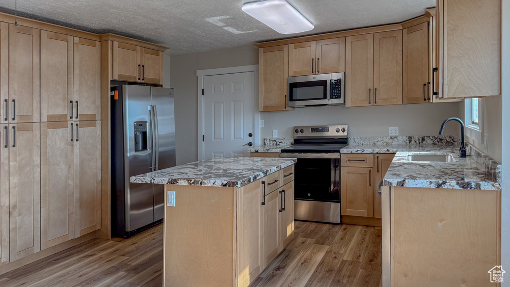 Kitchen featuring stainless steel appliances, light wood finished floors, light brown cabinets, light stone counters, and a textured ceiling
