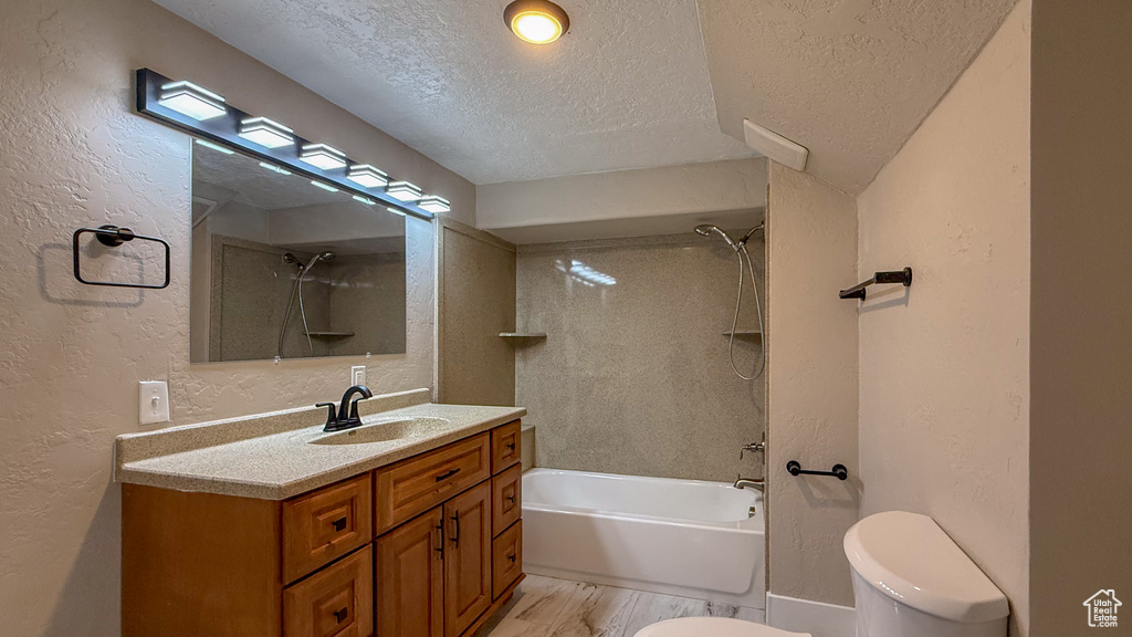 Bathroom with a textured ceiling, a textured wall, vanity, and shower / tub combination