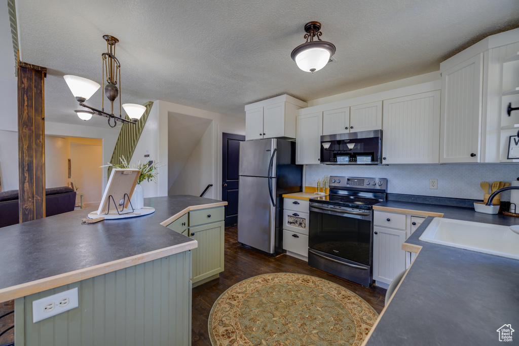 Kitchen with stainless steel appliances, dark countertops, white cabinetry, dark wood-type flooring, and a textured ceiling