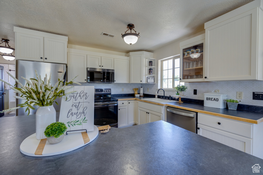 Kitchen featuring stainless steel appliances, dark countertops, white cabinetry, and a textured ceiling