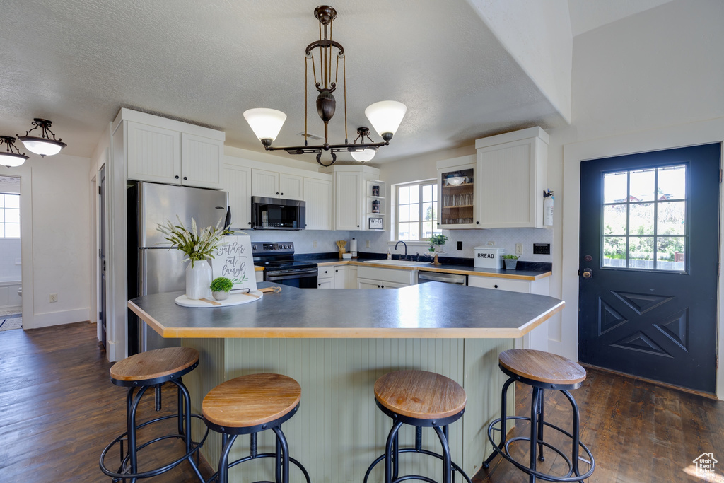 Kitchen with stainless steel appliances, white cabinetry, and dark wood-style flooring