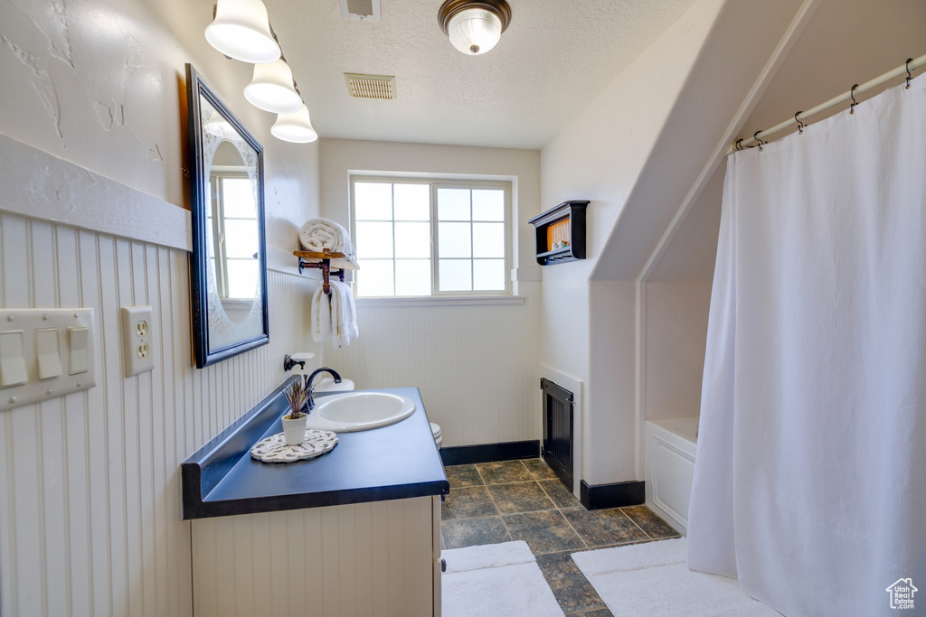 Full bath with vanity, wainscoting, a shower with shower curtain, stone finish flooring, and a textured ceiling