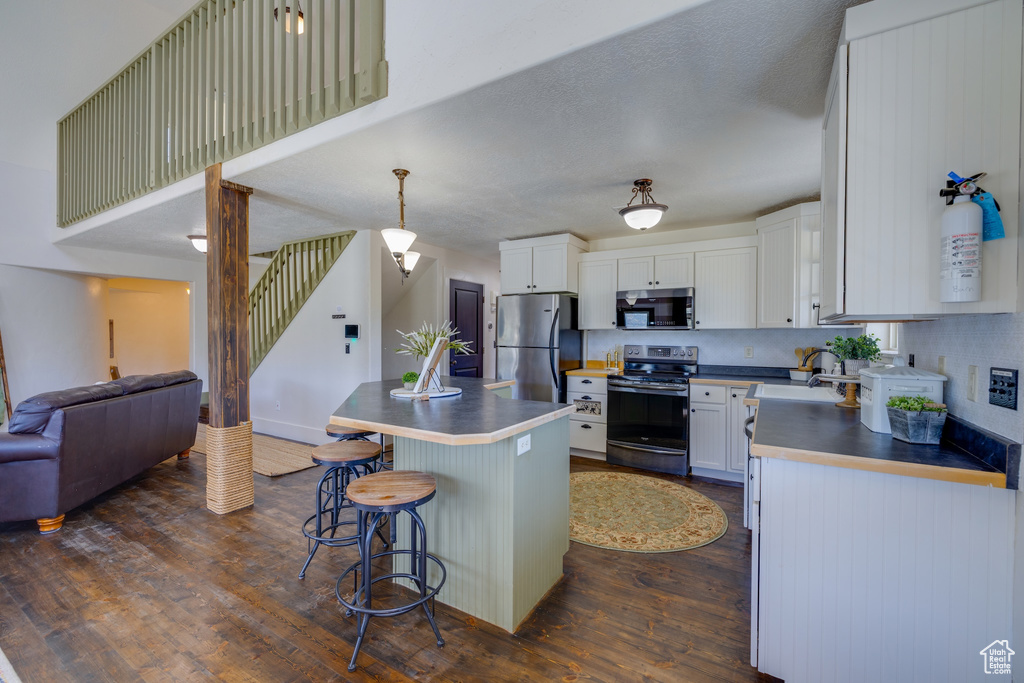 Kitchen featuring stainless steel appliances, open floor plan, dark wood-style flooring, a kitchen bar, and a center island