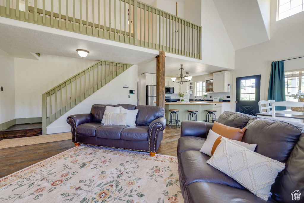 Living room with a high ceiling, wood finished floors, a chandelier, stairway, and healthy amount of natural light