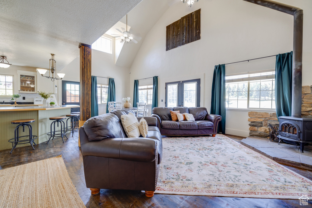 Living area featuring a wood stove, plenty of natural light, a chandelier, high vaulted ceiling, and a ceiling fan