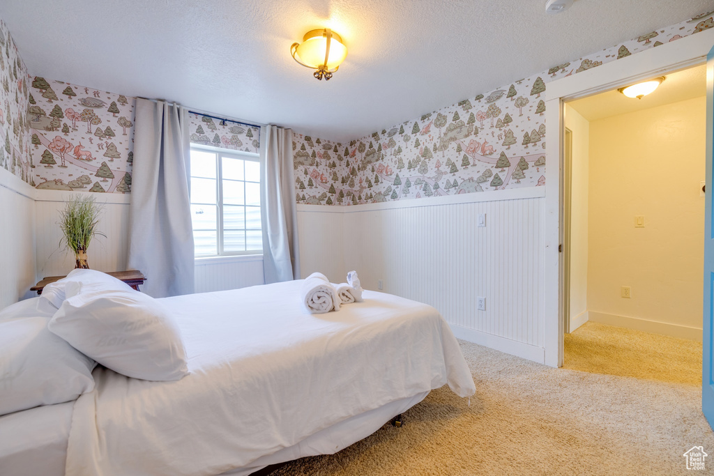 Carpeted bedroom with wallpapered walls, wainscoting, and a textured ceiling