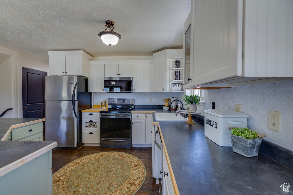 Kitchen featuring appliances with stainless steel finishes, dark countertops, white cabinetry, and a textured ceiling