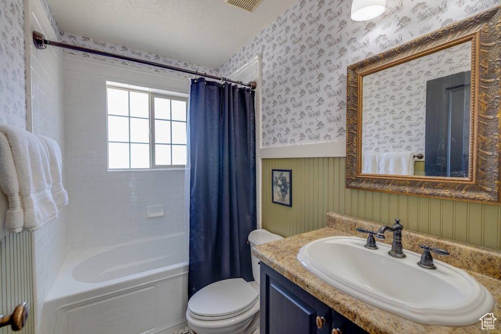 Bathroom featuring wallpapered walls, wainscoting, shower / bathtub combination with curtain, and vanity
