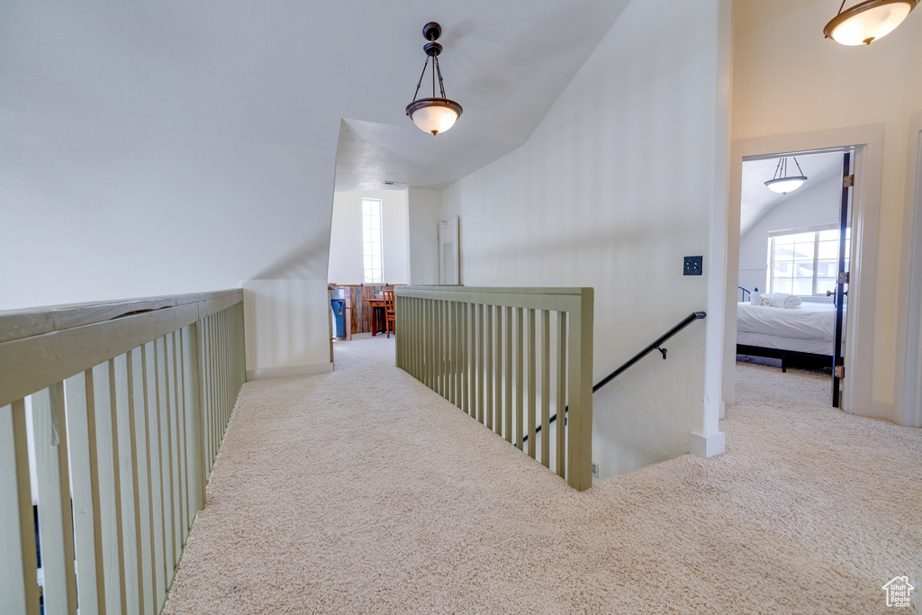 Corridor with carpet floors, vaulted ceiling, and an upstairs landing