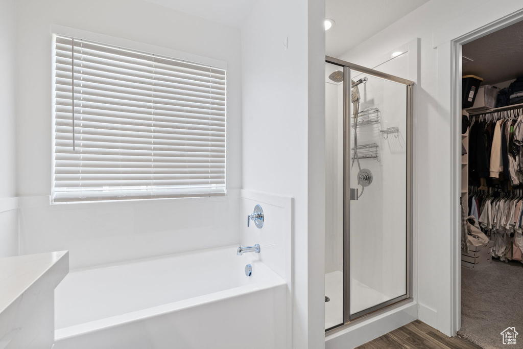 Full bathroom with a garden tub, a stall shower, a walk in closet, wood finished floors, and plenty of natural light