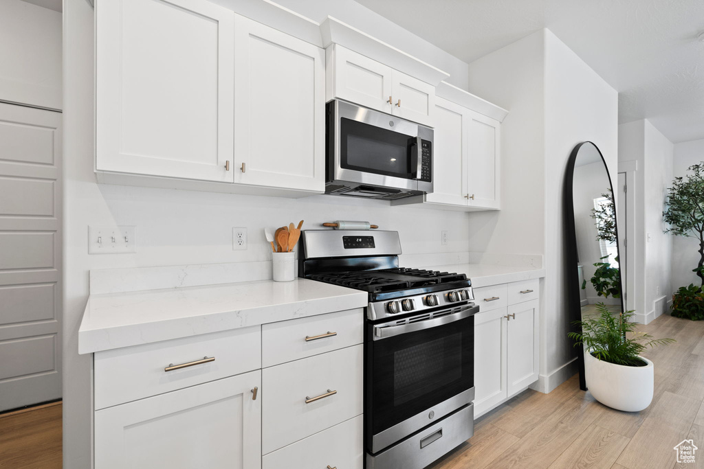 Kitchen with stainless steel appliances, light wood-type flooring, white cabinetry, and light stone countertops
