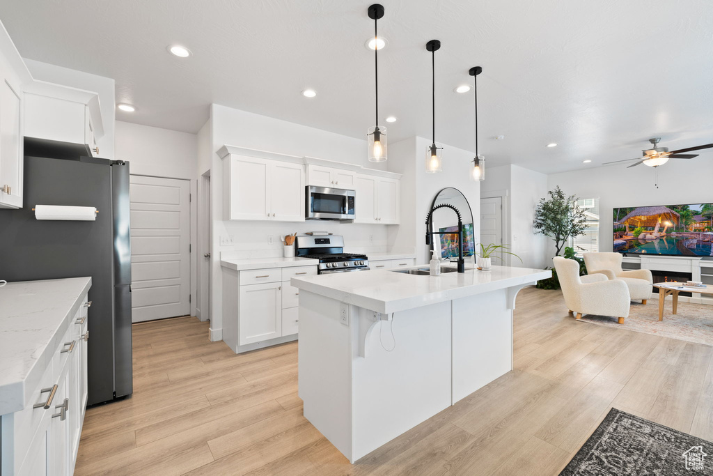 Kitchen with appliances with stainless steel finishes, a ceiling fan, open floor plan, light wood-style floors, and white cabinets