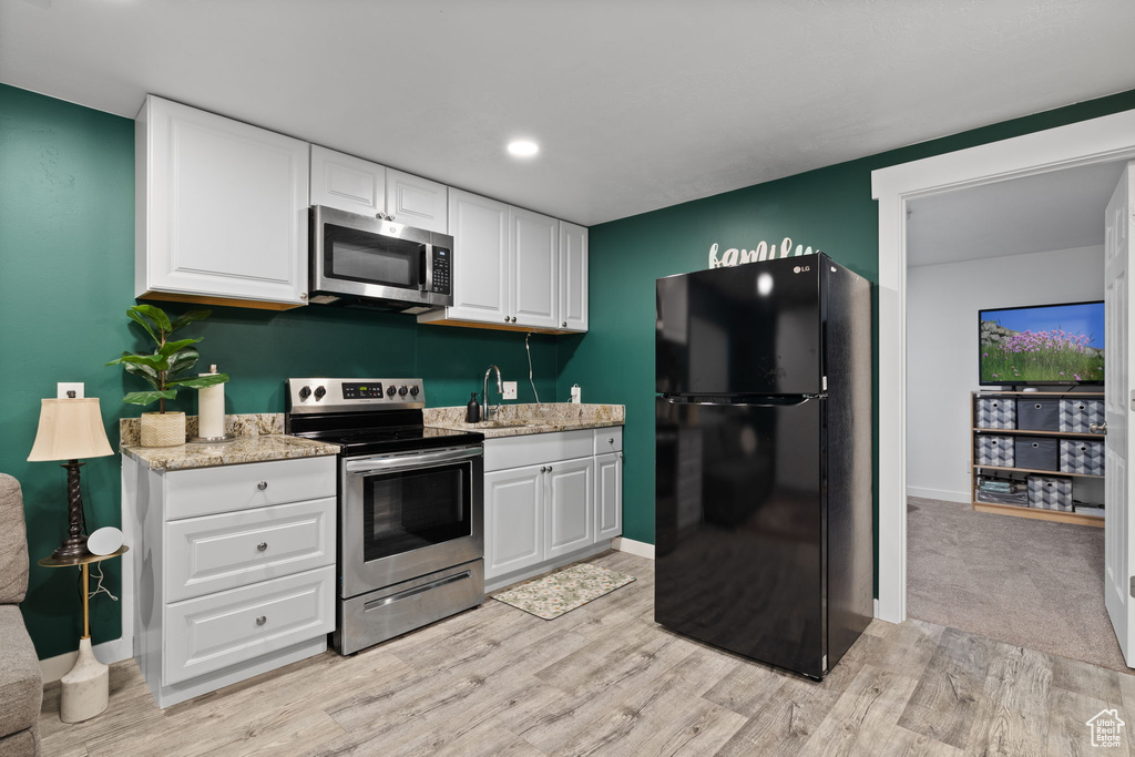 Kitchen with stainless steel appliances, light wood-type flooring, white cabinets, light stone counters, and recessed lighting