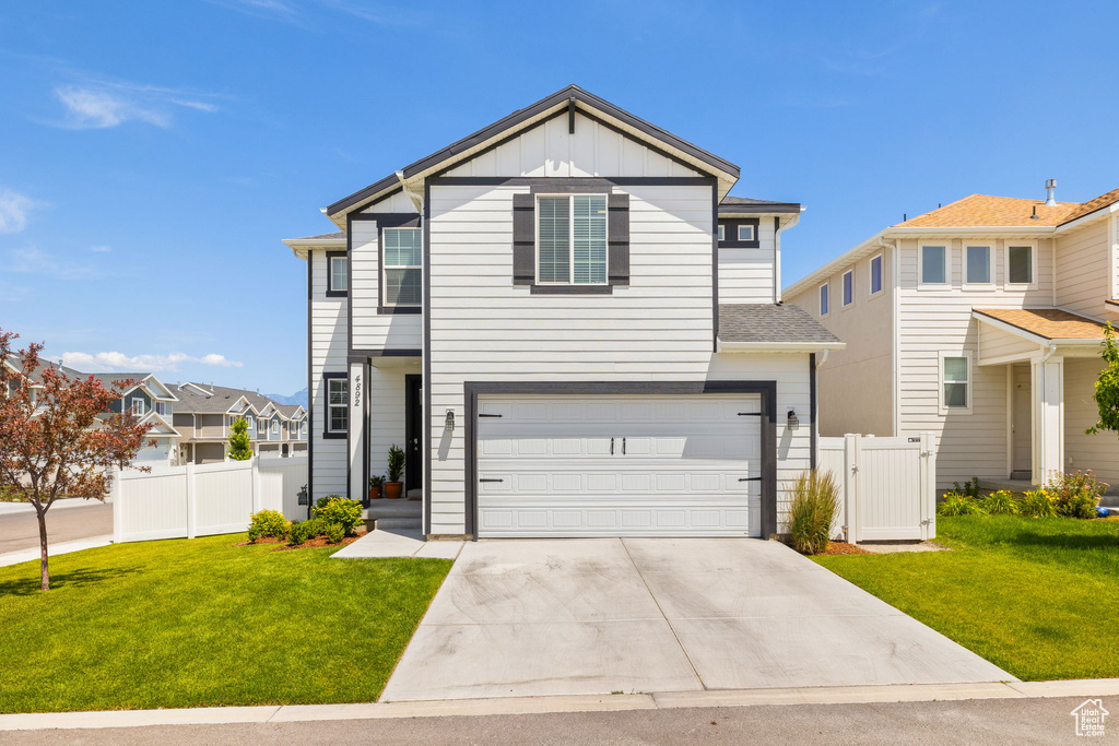 View of front facade with board and batten siding, concrete driveway, an attached garage, and a gate