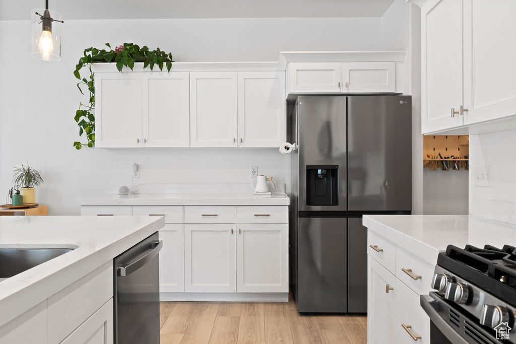 Kitchen featuring appliances with stainless steel finishes, white cabinetry, light wood finished floors, pendant lighting, and light stone countertops