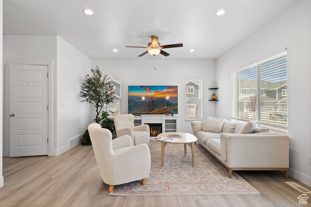 Living room featuring a ceiling fan, light wood-style floors, recessed lighting, and a warm lit fireplace