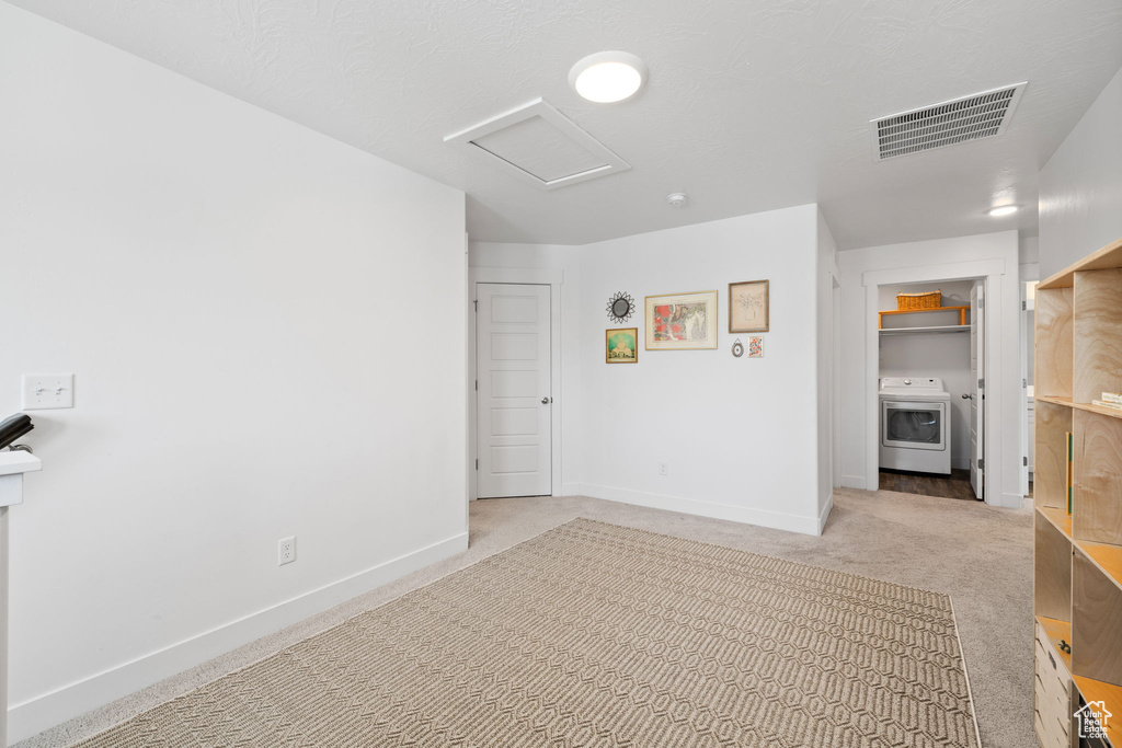 Empty room featuring attic access, washer / dryer, and light carpet