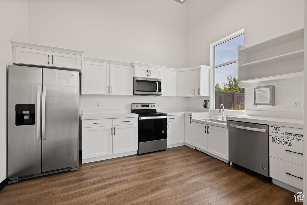 Kitchen featuring appliances with stainless steel finishes, a high ceiling, open shelves, white cabinetry, and light countertops