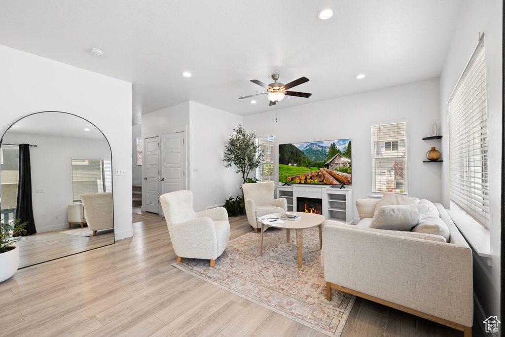 Living room featuring recessed lighting, plenty of natural light, light wood finished floors, a warm lit fireplace, and ceiling fan
