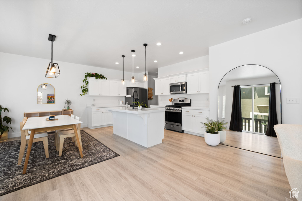 Kitchen featuring stainless steel appliances, light countertops, an island with sink, recessed lighting, and a breakfast bar area
