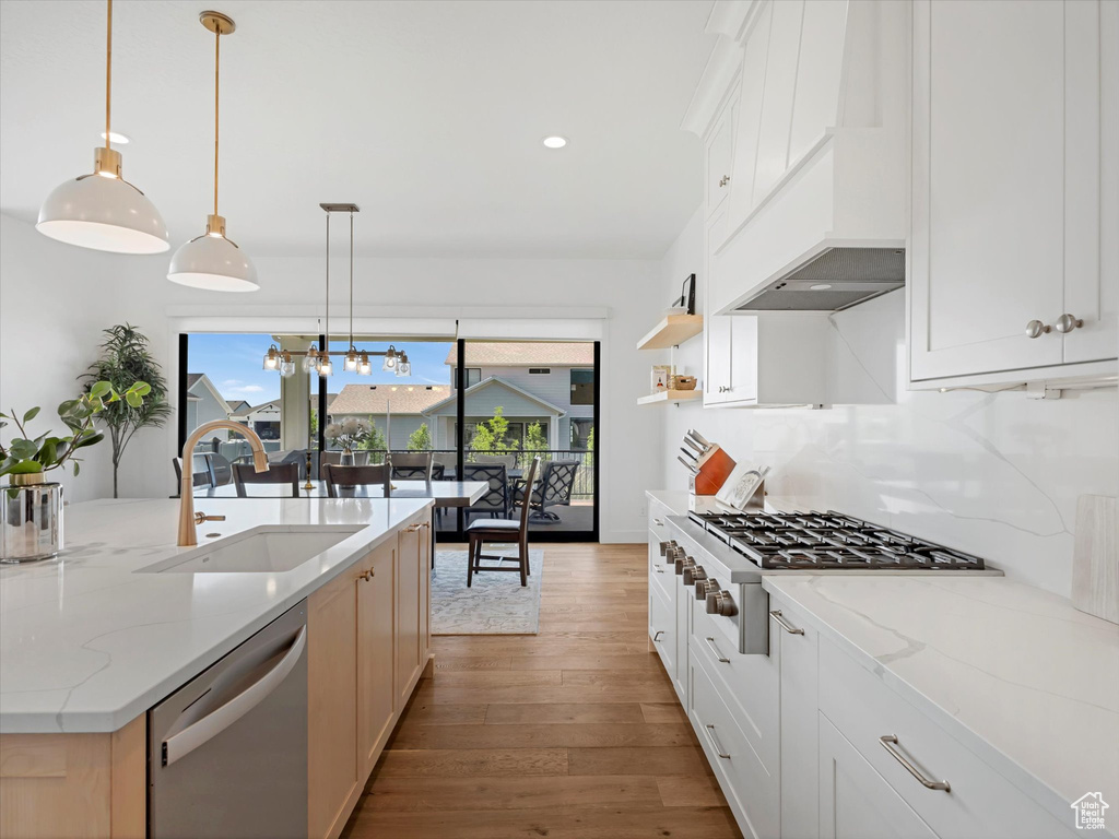 Kitchen with appliances with stainless steel finishes, wood finished floors, custom range hood, pendant lighting, and light stone countertops