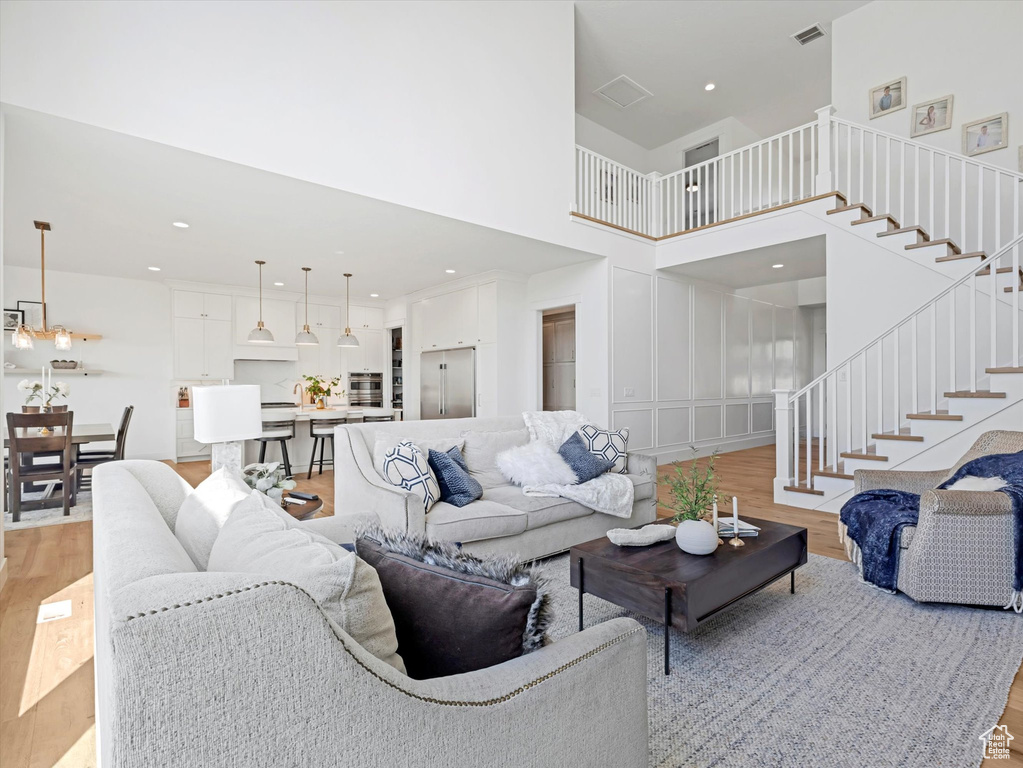 Living room featuring light wood-type flooring, stairs, a towering ceiling, and recessed lighting