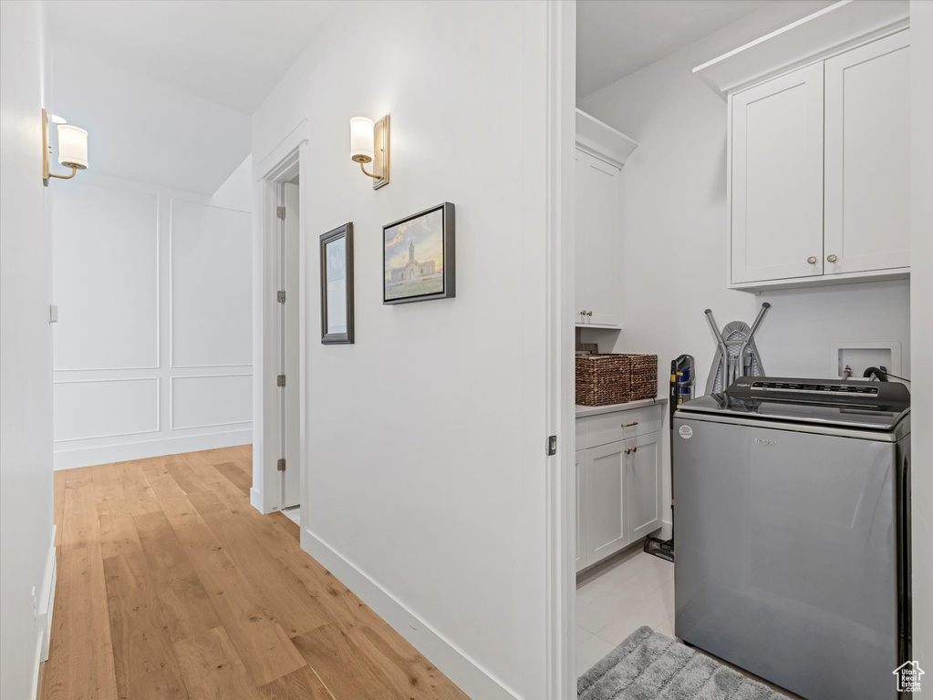 Washroom featuring washer / clothes dryer, cabinet space, and light wood-style flooring