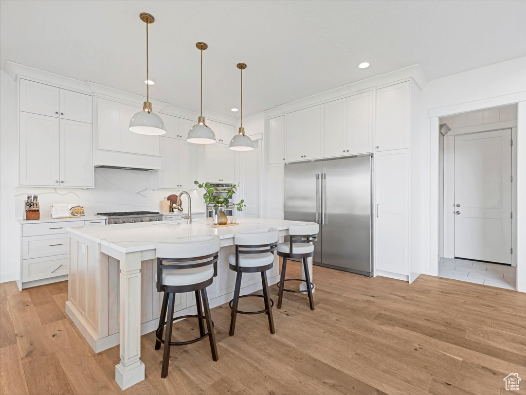Kitchen featuring built in fridge, light wood-type flooring, white cabinetry, light countertops, and a breakfast bar area