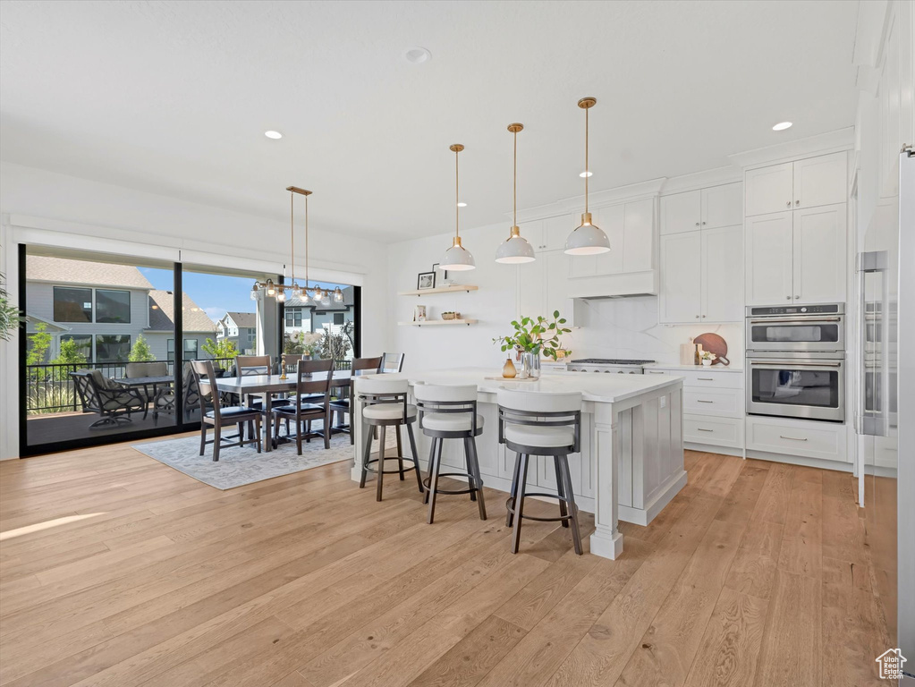 Kitchen featuring double oven, light countertops, white cabinetry, light wood finished floors, and recessed lighting