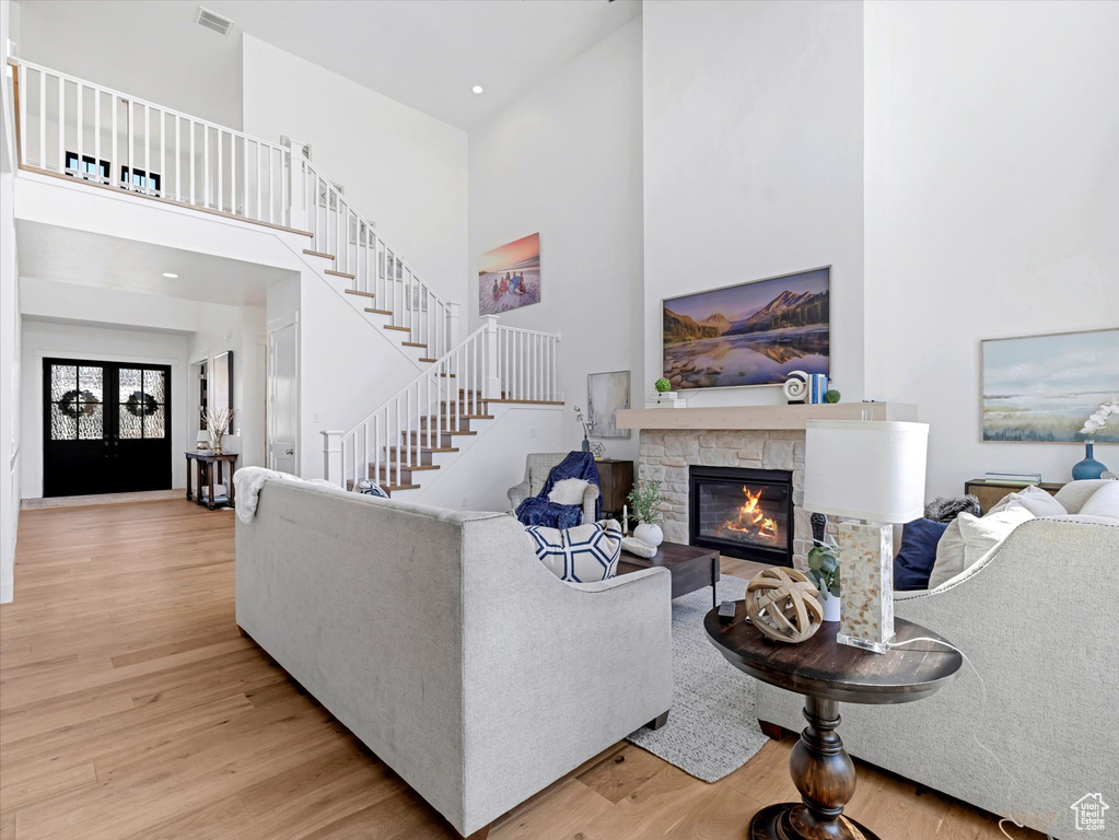 Living area with a high ceiling, light wood finished floors, a fireplace, stairs, and recessed lighting