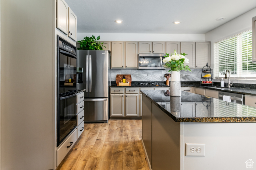 Kitchen featuring black appliances, light wood-style flooring, decorative backsplash, dark stone countertops, and recessed lighting