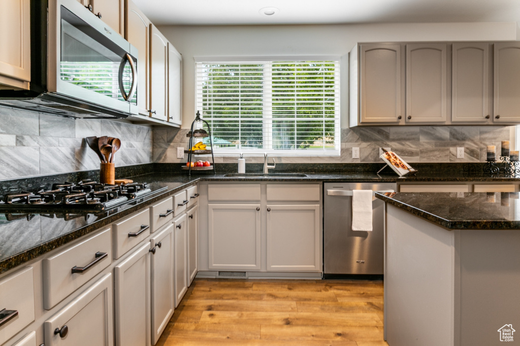 Kitchen with stainless steel appliances, light wood-style floors, decorative backsplash, and dark stone countertops