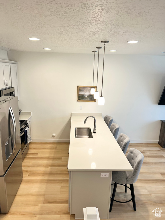 Kitchen with appliances with stainless steel finishes, a kitchen breakfast bar, a textured ceiling, recessed lighting, and decorative light fixtures