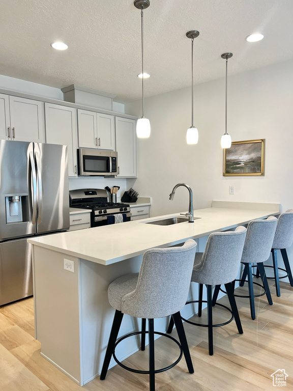 Kitchen featuring stainless steel appliances, a breakfast bar area, a peninsula, light wood-style flooring, and pendant lighting