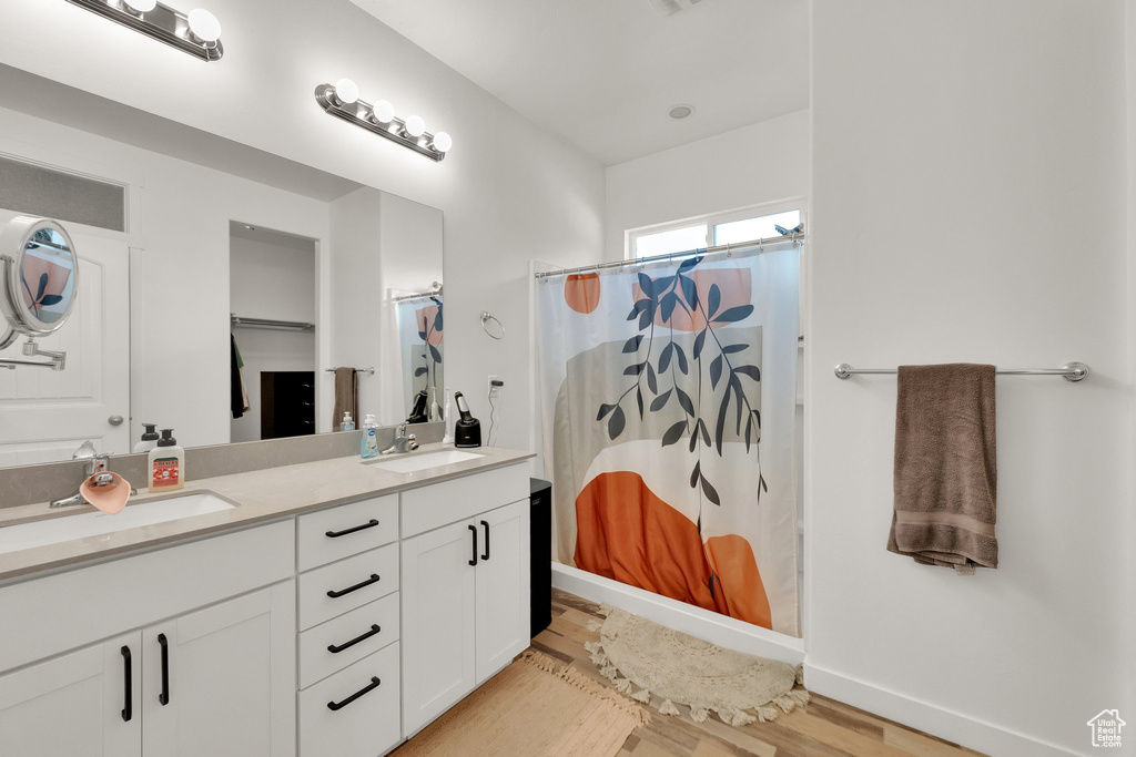 Full bath featuring wood finished floors, double vanity, and curtained shower