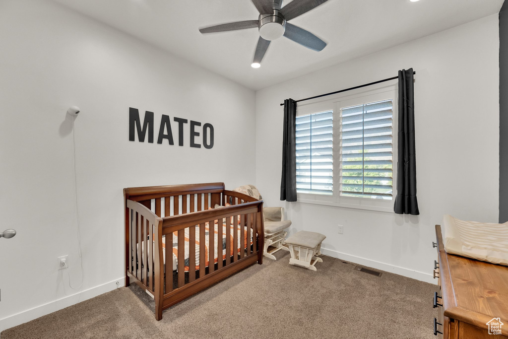 Carpeted bedroom with a crib and a ceiling fan