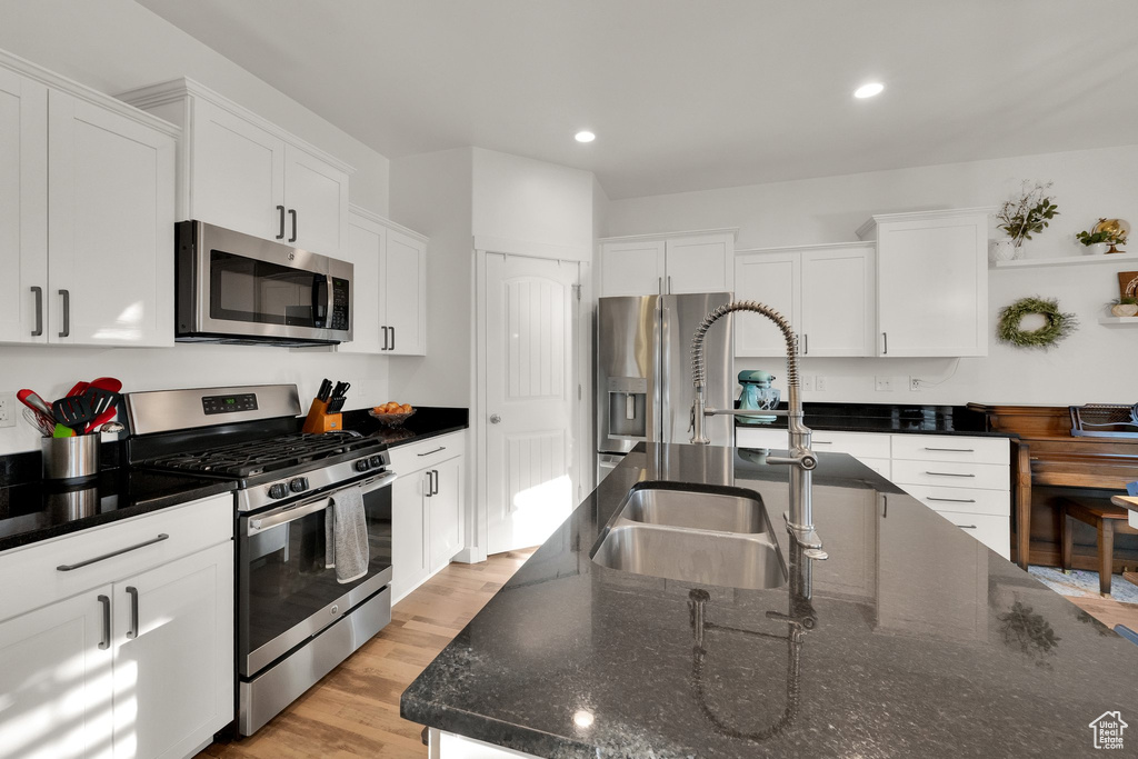Kitchen featuring stainless steel appliances, white cabinets, recessed lighting, light wood-type flooring, and dark stone countertops