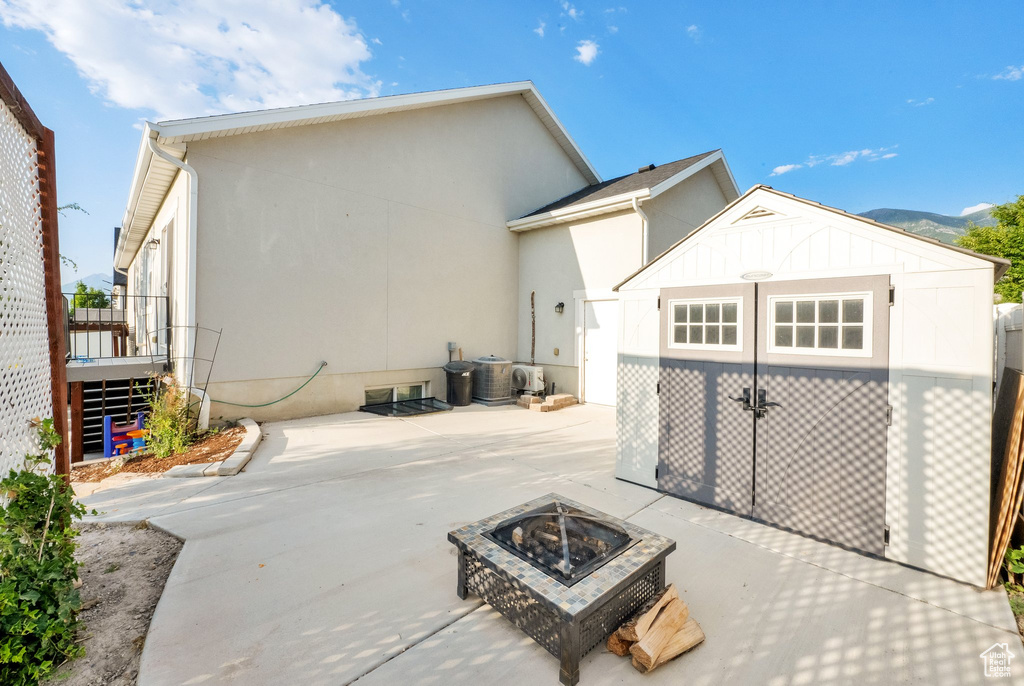 View of side of property with an outdoor fire pit, a patio, stucco siding, a shed, and driveway