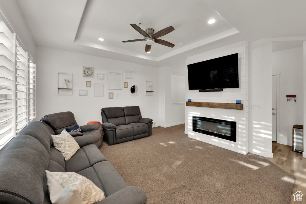 Living room featuring a raised ceiling, a ceiling fan, recessed lighting, a glass covered fireplace, and carpet