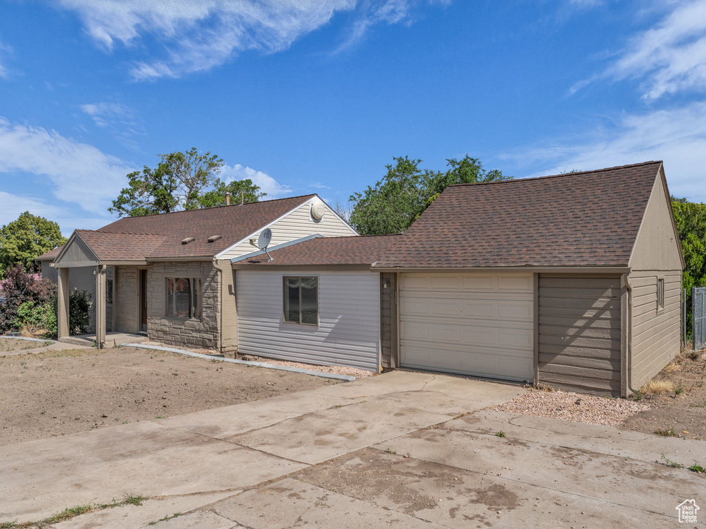 View of front of house featuring a garage, roof with shingles, driveway, and stone siding
