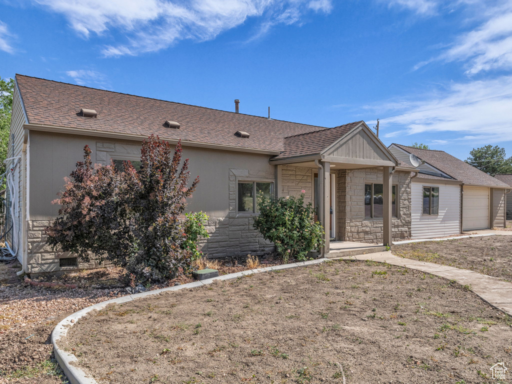 Ranch-style home featuring stone siding, an attached garage, and a shingled roof