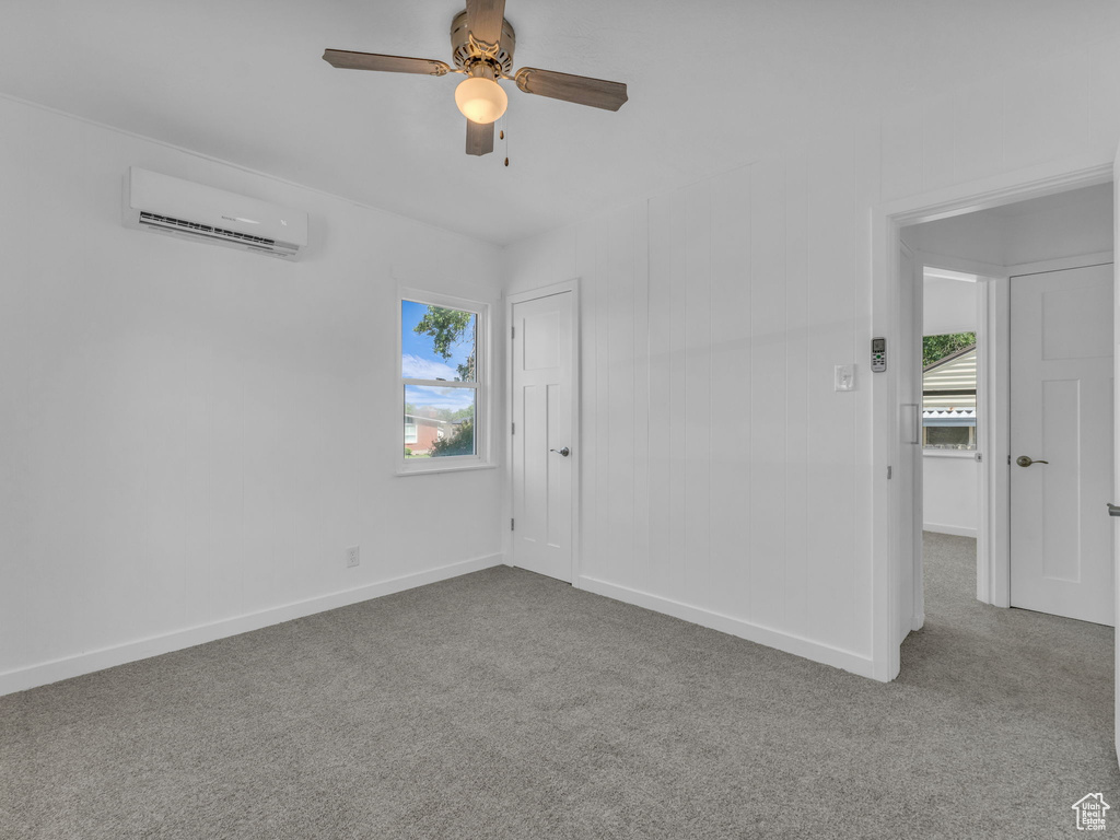 Unfurnished room featuring an AC wall unit, carpet floors, and a ceiling fan