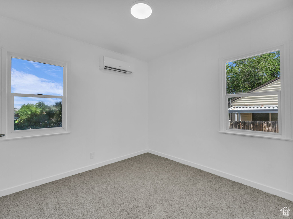 Carpeted spare room featuring a wall mounted AC and baseboards