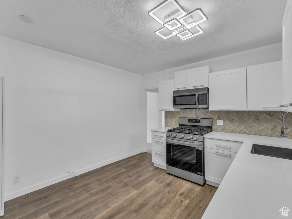 Kitchen with stainless steel appliances, a textured ceiling, backsplash, light countertops, and white cabinets