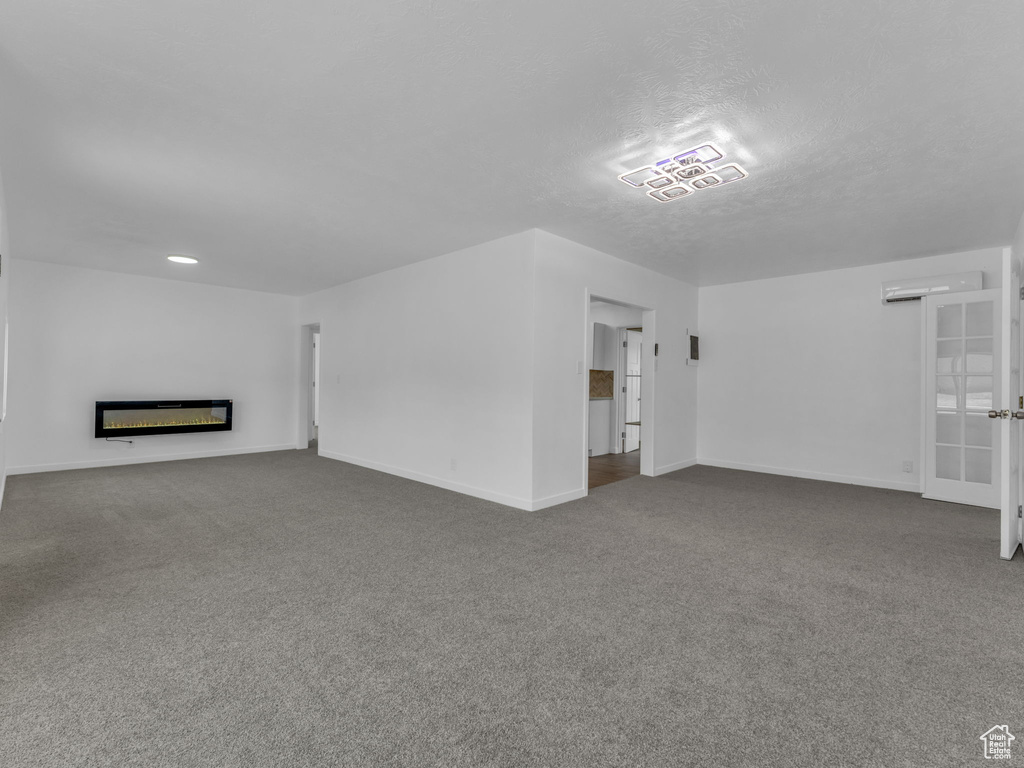 Unfurnished living room featuring dark colored carpet, a glass covered fireplace, and a textured ceiling