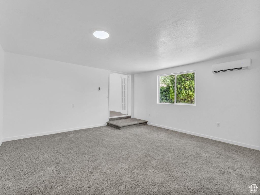 Unfurnished room featuring a wall unit AC, carpet flooring, and a textured ceiling