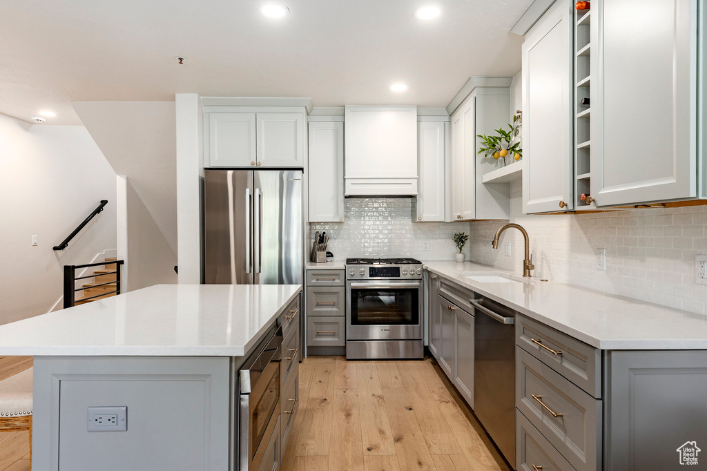 Kitchen with appliances with stainless steel finishes, gray cabinets, light wood-type flooring, a kitchen island, and recessed lighting