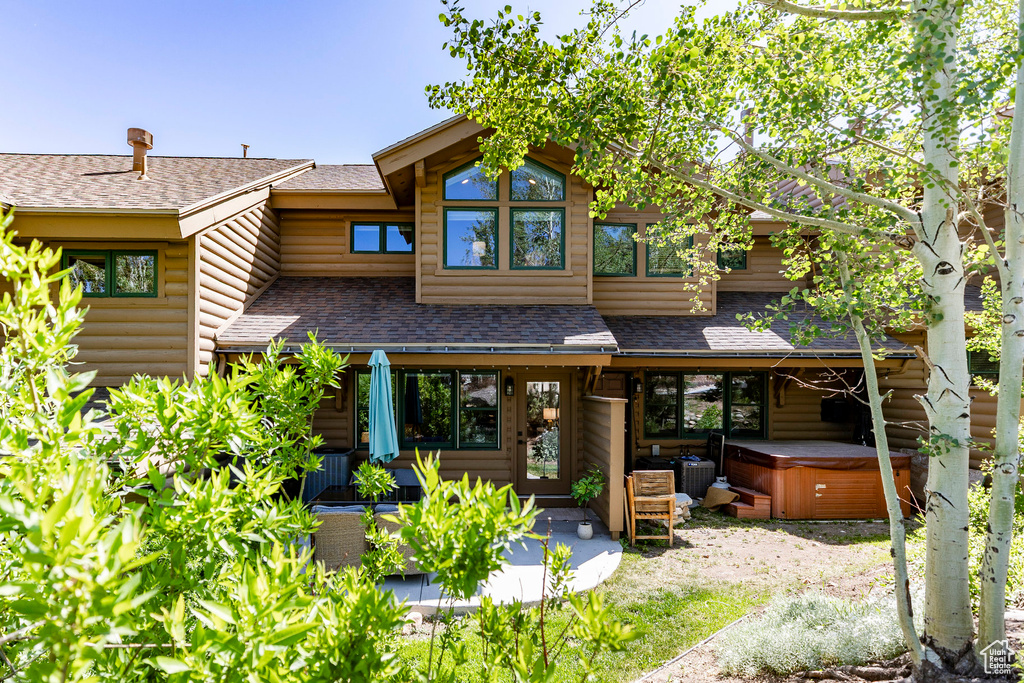 Back of house with a hot tub, roof with shingles, log veneer siding, and a patio area